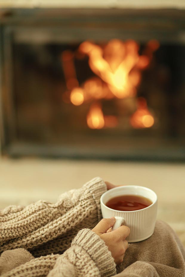 femme assise dans un fauteil avec une tasse de the et une chemine